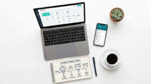 Flat-lay workspace showing laptop with email automation workflow, smartphone with CRM contacts, and notebook with customer journey funnel sketches on a clean white desk